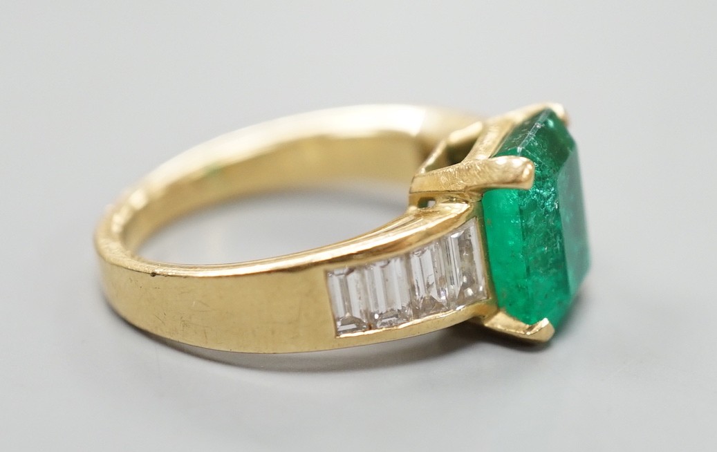 A modern yellow metal and single stone emerald set dress ring, with graduated baguette cut diamond set shoulders, size M/N, gross weight 7.3 grams.